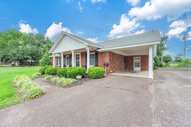 Greek revival house featuring brick siding, asphalt driveway, an attached carport, and covered porch