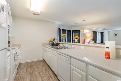 Kitchen featuring hanging light fixtures, white cabinetry, light wood-type flooring, sink, and white appliances