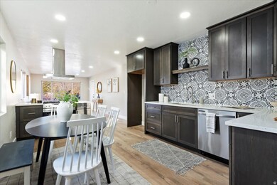 Kitchen featuring backsplash, stainless steel appliances, light wood-type flooring, light stone counters, and wall chimney range hood
