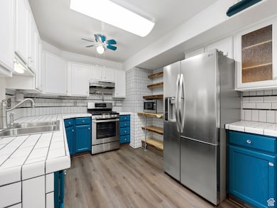 Kitchen featuring blue cabinets, tasteful backsplash, tile counters, and stainless steel appliances
