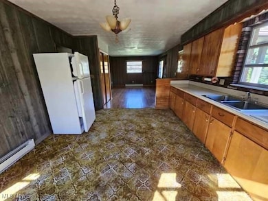 Kitchen featuring wood walls, brown cabinetry, freestanding refrigerator, light countertops, and a baseboard radiator