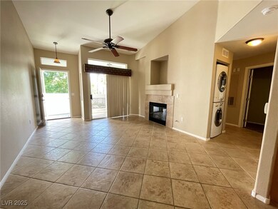 Unfurnished living room with a tiled fireplace, stacked washer and clothes dryer, a ceiling fan, and light tile patterned floors