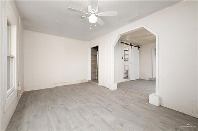 Empty room featuring a ceiling fan, a barn door, wood finished floors, and arched walkways