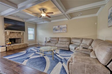 Living area featuring wood finished floors, coffered ceiling, ceiling fan, beam ceiling, and a fireplace