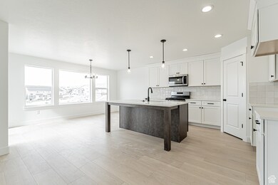 Kitchen with a kitchen bar, a center island with sink, white cabinets, decorative backsplash, and appliances with stainless steel finishes