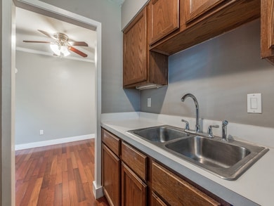 Kitchen featuring dark wood-type flooring, brown cabinets, ornamental molding, a ceiling fan, and light countertops