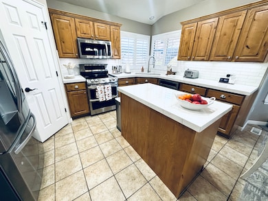 Kitchen featuring decorative backsplash, a center island, stainless steel appliances, brown cabinetry, and light tile patterned floors