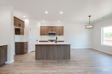 Kitchen featuring brown cabinets, hanging light fixtures, a center island with sink, recessed lighting, and light wood-style flooring