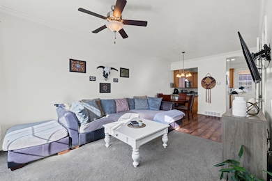Living room with ornamental molding, a chandelier, wood finished floors, and a ceiling fan
