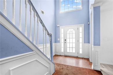 Carpeted foyer entrance with a high ceiling, wainscoting, and stairs