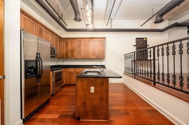 Kitchen with stainless steel appliances, dark countertops, dark wood-style flooring, and brown cabinetry