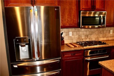 Kitchen with stainless steel appliances, dark brown cabinets, light stone counters, and decorative backsplash