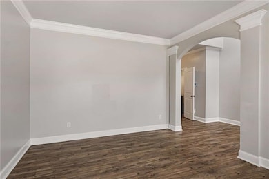 Unfurnished room with crown molding, dark wood-style floors, arched walkways, and baseboards