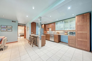 Kitchen featuring a kitchen breakfast bar, glass insert cabinets, brown cabinetry, decorative backsplash, and light tile patterned flooring