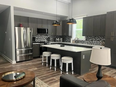 Kitchen featuring appliances with stainless steel finishes, a kitchen island, light countertops, a breakfast bar, and dark wood finished floors