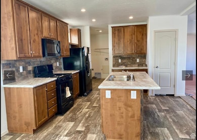 Kitchen with brown cabinetry, black appliances, a kitchen island with sink, light countertops, and a textured ceiling