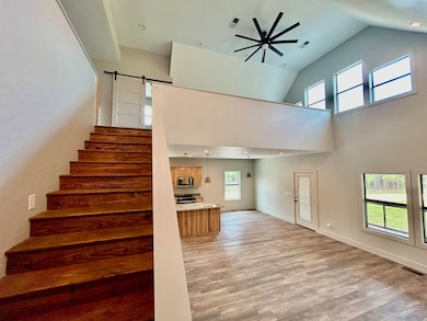 Stairway with wood finished floors, ceiling fan, a barn door, high vaulted ceiling, and recessed lighting