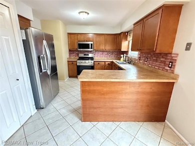Kitchen featuring a peninsula, light tile patterned flooring, appliances with stainless steel finishes, and brown cabinetry