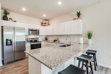 Kitchen featuring stainless steel appliances, a sink, a peninsula, light wood-style flooring, and backsplash