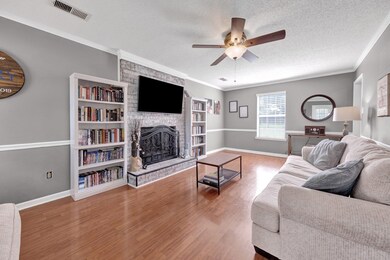 Living area with a stone fireplace, ceiling fan, wood finished floors, a textured ceiling, and baseboards