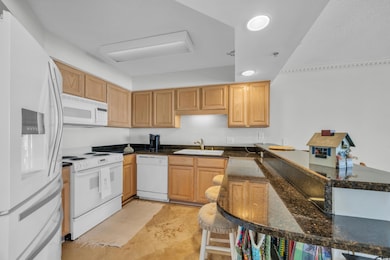 Kitchen with white appliances, a sink, dark stone countertops, and a peninsula