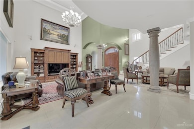 Living room featuring ornate columns, a high ceiling, stairway, a chandelier, and tile patterned floors