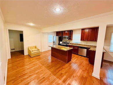 Kitchen featuring ornamental molding, light stone countertops, light wood-style floors, a center island, and stainless steel appliances