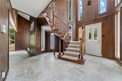 Entrance foyer with wood walls, healthy amount of natural light, stairway, and a towering ceiling