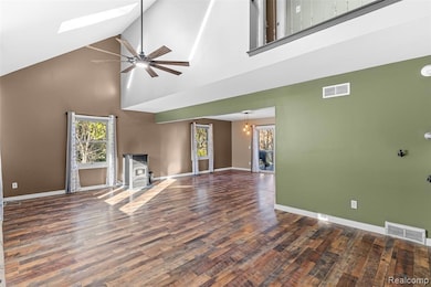 Unfurnished living room featuring a wood stove, high vaulted ceiling, ceiling fan, dark wood-type flooring, and a skylight