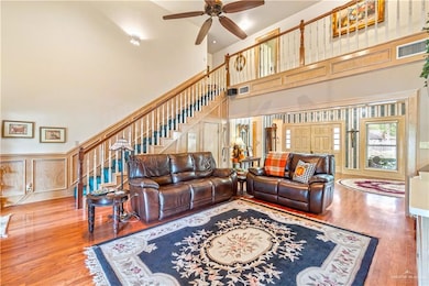 Living room with ceiling fan, wood-type flooring, and a towering ceiling