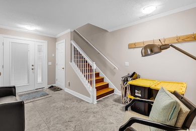 Foyer entrance featuring a textured ceiling, crown molding, and stairs
