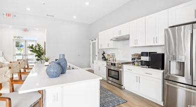 Kitchen featuring appliances with stainless steel finishes, tasteful backsplash, light wood-style flooring, light countertops, and white cabinetry