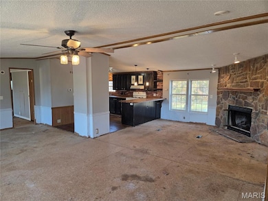 Unfurnished living room with a wainscoted wall, a stone fireplace, ornamental molding, ceiling fan, and a textured ceiling