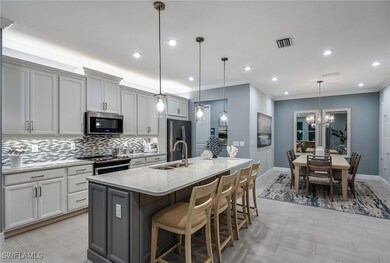 Kitchen featuring a breakfast bar area, light stone countertops, a center island with sink, gray cabinetry, and pendant lighting