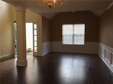 Spare room with ornate columns, dark wood-type flooring, a chandelier, lofted ceiling, and a wainscoted wall