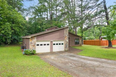 View of side of home featuring stone siding, a garage, driveway, and cooling unit