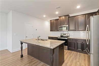 Kitchen with stainless steel appliances, tasteful backsplash, light stone counters, dark brown cabinets, and light wood finished floors