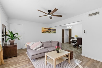 Living room featuring a ceiling fan, light wood-style floors, ornamental molding, a chandelier, and a textured ceiling