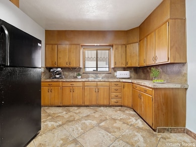 Kitchen featuring freestanding refrigerator, light countertops, brown cabinets, backsplash, and a textured ceiling