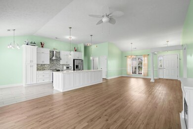 Unfurnished living room featuring lofted ceiling, a chandelier, a ceiling fan, light wood-style floors, and baseboards