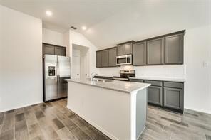 Kitchen with wood-type flooring, a kitchen island with sink, stainless steel appliances, sink, and lofted ceiling