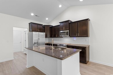 Kitchen featuring appliances with stainless steel finishes, dark stone counters, light wood-type flooring, dark brown cabinets, and lofted ceiling