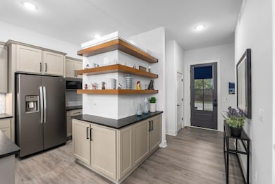 Kitchen featuring open shelves, stainless steel refrigerator with ice dispenser, light wood-style floors, dark stone counters, and recessed lighting