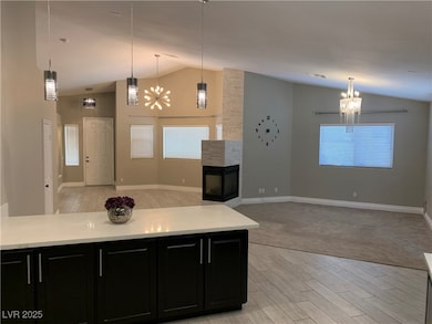 Kitchen featuring dark cabinets, a chandelier, open floor plan, light wood-type flooring, and high vaulted ceiling