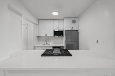 Kitchen featuring white cabinets, backsplash, appliances with stainless steel finishes, light stone countertops, and a peninsula