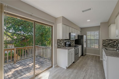 Kitchen featuring stainless steel appliances, decorative backsplash, white cabinetry, light wood-style flooring, and recessed lighting