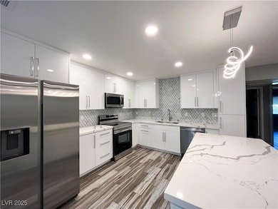 Kitchen featuring stainless steel appliances, hanging light fixtures, modern cabinets, light stone counters, and white cabinetry
