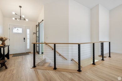 Foyer featuring a barn door, a chandelier, light wood-type flooring, and lofted ceiling