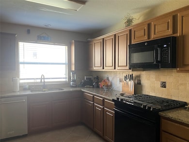 Kitchen featuring black appliances, dark tile patterned floors, dark stone counters, and backsplash