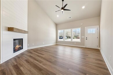 Unfurnished living room with high vaulted ceiling, wood finished floors, ceiling fan, a large fireplace, and baseboards